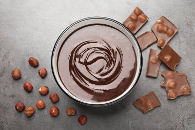 Erimiş çikolata kasede, parçalar ve fındıklar gri masada, düz yerde
