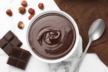 Erimiş çikolata kasede, parçalarda, fındıkta ve kaşıkta beyaz mermer masada, düz yerde.