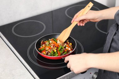 Kızartma tavasında taze sebze ve ahşap spatula karıştıran kadın, yakın plan.