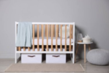 Beşik, depolama kutuları, masa ve açık gri duvarın yanındaki puf. Şık bir bebek odası.