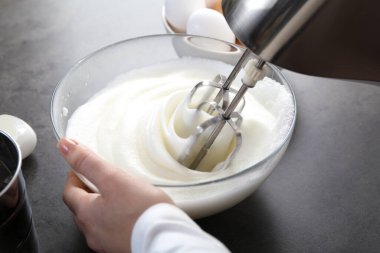 Gri masada yumurta beyazını mikserle döven kadın, yakın plan.