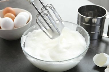 Gri masada yumurta beyazını mikserle çırpmak, yakın plan.