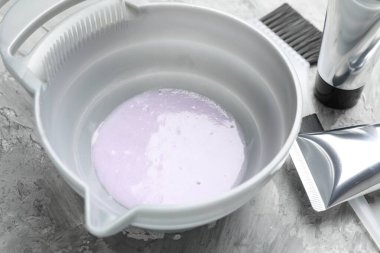 Tabaktaki saç boyama ürünü ve açık gri masadaki farklı kuaför aletleri.