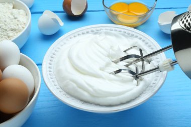 Kasede çırpılmış yumurta beyazı, mikser ve ürünler mavi ahşap masada, yakın plan.