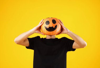 Cadılar Bayramı kutlaması. Turuncu arka planda çizilmiş ürkütücü yüzü olan bir adam balkabağı tutuyor.