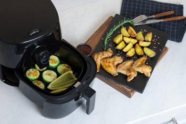 Beyaz mermer tezgahta ızgara sebzeli, tavuk kanatlı, patates dilimli ve baharatlı kızartma makinesi.