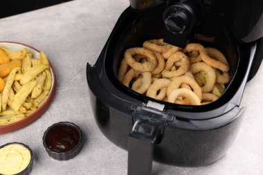 Lezzetli kalamar halkalı kızartma, tavuk nugget, patates kızartması ve soslar gri masada, yakın plan.