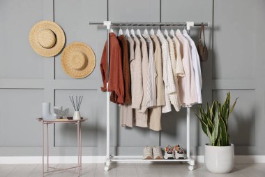 Kadın kıyafetleri askıda, şapkalarda, ev bitkilerinde ve kahve masasında asılı.