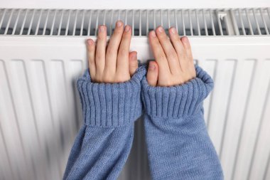 Kadın ellerini radyatörün yanında ısıtıyor, yakın plan.