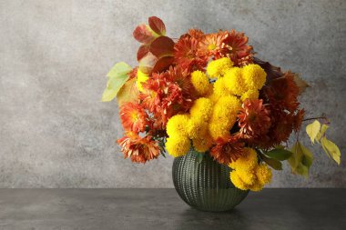 Sonbahar atmosferi. Güzel çiçekli vazo ve gri masada yapraklar, metin için boşluk