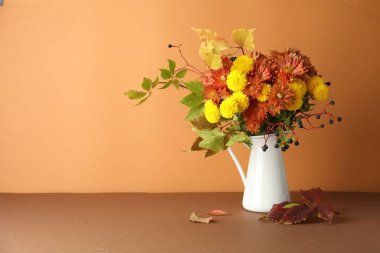 Sonbahar atmosferi. Güzel çiçekli vazo, böğürtlen ve yapraklar kahverengi masada turuncu arka planda, metin için boşluk