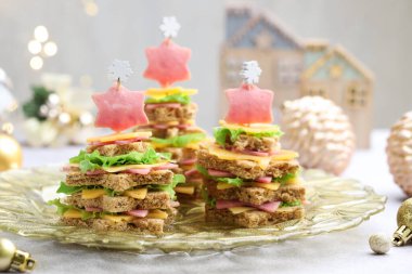 Noel yemeği. Ekmek, peynir, jambon, marul ve dekordan yapılmış fidan ağaçları açık gri masada arka planda bulanık ışıklarla, yakın plan. Bokeh etkisi