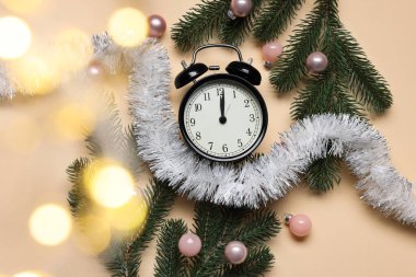 Yeni yıl tebrik kartı. Alarm saati, köknar ağacı dalları, bej arka planda takılar ve süsler, düz bir zemin. Bokeh etkisi