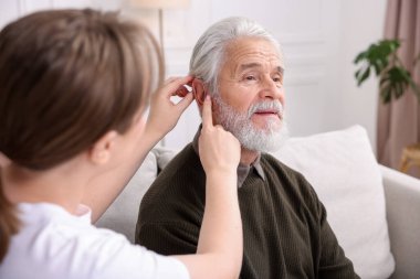 Bakıcı, kıdemli adamın evde işitme cihazı takmasına yardım ediyor.