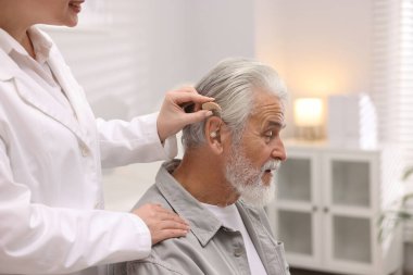 Doktor hastanede yaşlı adamın kulağına işitme cihazı takıyor.