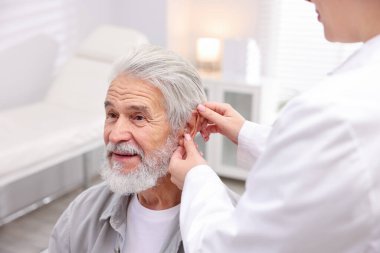 Doktor hastanede yaşlı adamın kulağına işitme cihazı takıyor.