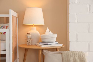 Şık bebek odasında beşik, masa, lamba ve dekor.