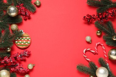 Kırmızı arka planda köknar ağacı dalları, Noel dekorasyonu, kurabiye ve şeker kamışları olan düz bir kompozisyon. Metin için boşluk