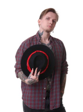 Piercingli, dövmeli ve beyaz arka planda poz veren şık elbiseli genç bir adam.