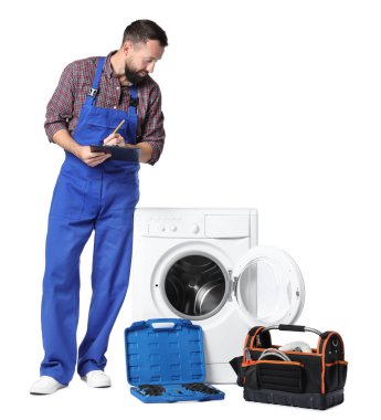 Beyaz arka planda bozuk çamaşır makinesinin yanında panosu olan profesyonel bir tamirci.