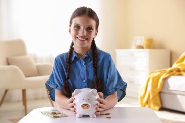 Domuz kumbarası ve cep harçlığı olan gülümseyen küçük bir kız.