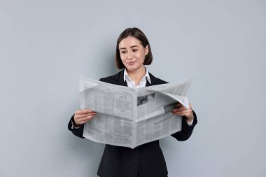 Takım elbiseli güzel kadın gri arka planda gazete okuyor.