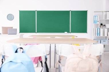 Sınıfta yeşil karatahta, masalar ve sandalyeler var. Tasarım için model