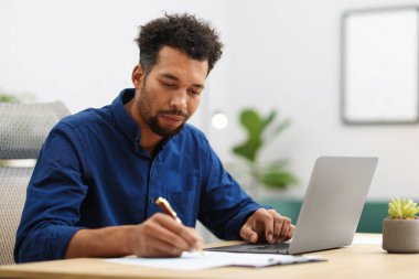 Bilgisayarla çalışan ve ofiste yazı yazan bir adam.