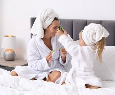 Havlu ve salatalık dilimli bornozlu bir anne ve kız evde yataktalar.