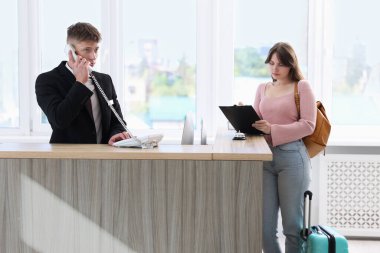 İçerideki resepsiyonda misafir ile çalışan resepsiyonist.