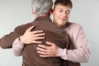 Baba ve oğul açık gri arka planda sarılıyorlar.