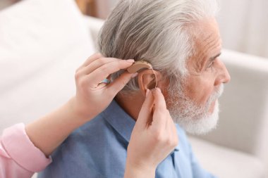 Bakıcı, kıdemli adamın evde işitme cihazı takmasına yardım ediyor.