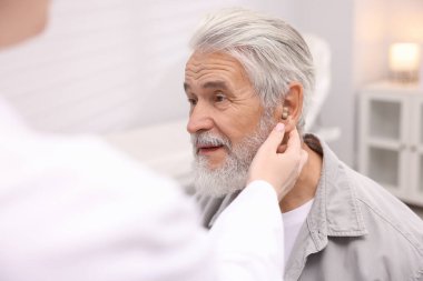 Doktor hastanede yaşlı adamın kulağına işitme cihazı takıyor.