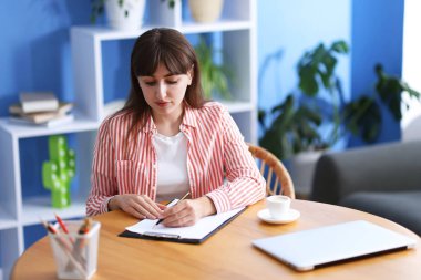 Kahve molası. Güzel bir kadın, kapalı bir masada, bardağın yanında yazıyor.