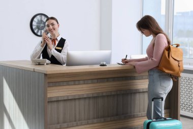 İçerideki resepsiyonda misafir ile çalışan resepsiyonist.