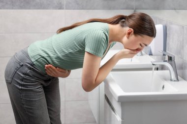 Banyoda mide ağrısı ve mide bulantısı çeken bir kadın.