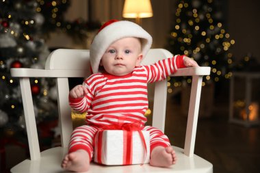 Noel Baba şapkalı şirin bebek ve evde Noel hediyesi olan parlak pijamalar.