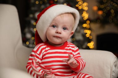 Noel Baba şapkalı şirin bebek ve elinde baston şeker tutan parlak Noel pijamaları.