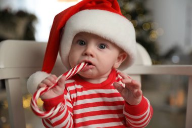 Noel Baba şapkalı şirin bebek ve evde şeker yiyen parlak Noel pijamaları.