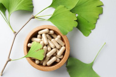 Ginkgo biloba yaprakları ve açık gri arka planda bir kase hap.