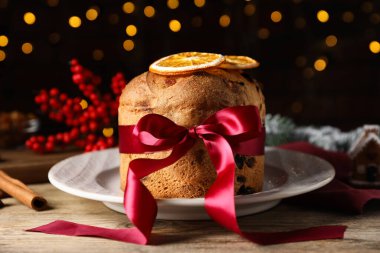 Noel yemeği. Lezzetli Panettone pastası, baharatlar ve ahşap masanın üzerindeki şenlikli dekor. Arka planda bulanık ışıklar, yakın plan. Bokeh etkisi