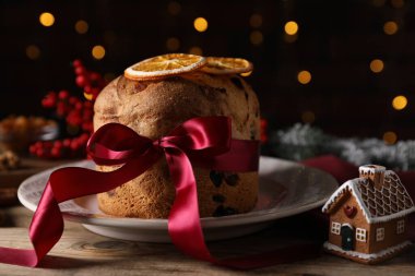 Noel yemeği. Lezzetli Panettone pastası, malzemeler, zencefilli kek evi ve ahşap masa üzerindeki şenlikli dekor arka planda bulanık ışıklar, yakın plan. Bokeh etkisi