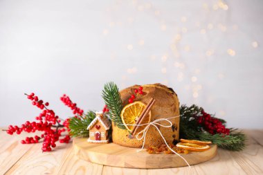 Noel yemeği. Lezzetli Panettone pastası, malzemeler, zencefilli kek evi ve ahşap masa üzerindeki şenlikli dekor arka planda bulanık ışıklar, yakın plan. Bokeh etkisi