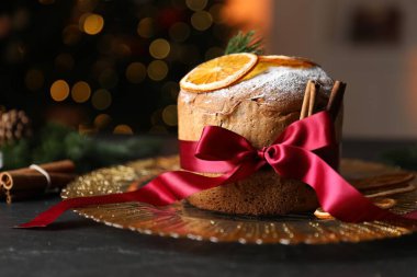 Noel yemeği. Lezzetli Panettone pastası, baharatlar ve siyah masanın üzerinde arka planda bulanık ışıklar, yakın plan. Bokeh etkisi