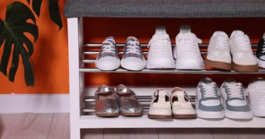 Kapalı alandaki turuncu duvarın yanındaki depodaki farklı çocukların ayakkabıları. Kamera sağa hareket ediyor