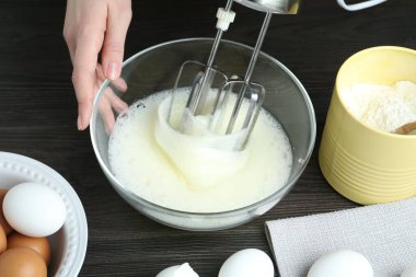 Siyah ahşap masada yumurta beyazlarını el çırpıcı ile çırpan kadın, yakın plan.