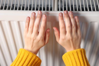 Kadın ellerini radyatörün yanında ısıtıyor, yakın plan.