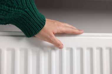 Kadın elini radyatörün yanında ısıtıyor, yakın plan.