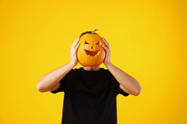 Cadılar Bayramı kutlaması. Turuncu arka planda oyulmuş ürkütücü yüzü olan bir adam balkabağı tutuyor.