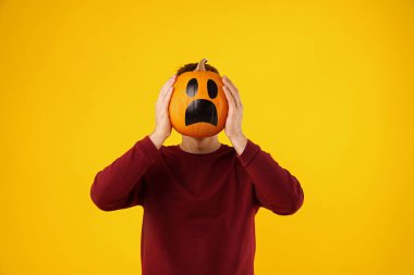 Cadılar Bayramı kutlaması. Turuncu arka planda çizilmiş ürkütücü yüzü olan bir adam balkabağı tutuyor.